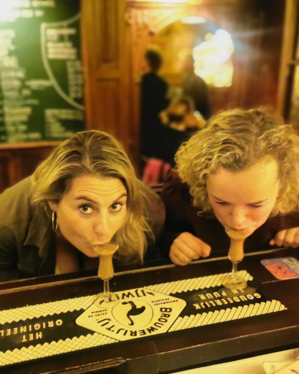 Guests taking the traditional first sip of jenever, bent over the bar in an Amsterdam cafe